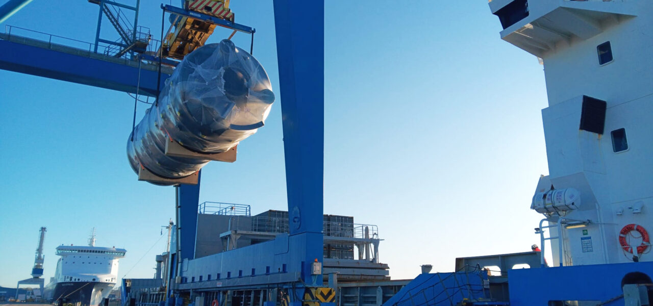 Oversized cylindrical cargo under crane lift at quay, transferred between vessel and port during project logistics handling