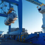 Oversized cylindrical cargo under crane lift at quay, transferred between vessel and port during project logistics handling