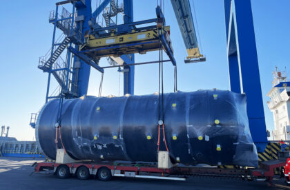 Large cylindrical industrial unit being lifted by crane onto trailer at port during project cargo handling