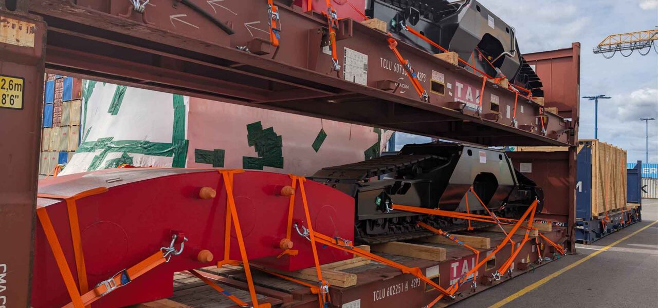 Detailed view of heavy equipment and components secured on flat racks using lashing and dunnage to ensure safe international transport.