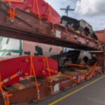 Detailed view of heavy equipment and components secured on flat racks using lashing and dunnage to ensure safe international transport.