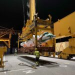 Container crane handling project cargo during vessel loading operations, highlighting specialized logistics and port expertise for heavy-lift shipments.