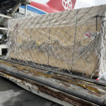 Large industrial shipment secured with cargo netting during aircraft loading operations.