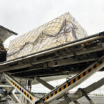 Heavy industrial unit prepared for international air freight shipment and loaded onto an aircraft cargo loader.