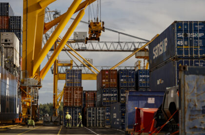 Container handling operations at a Finnish cargo terminal with gantry cranes, stacked shipping containers, and a container vessel alongside the quay.