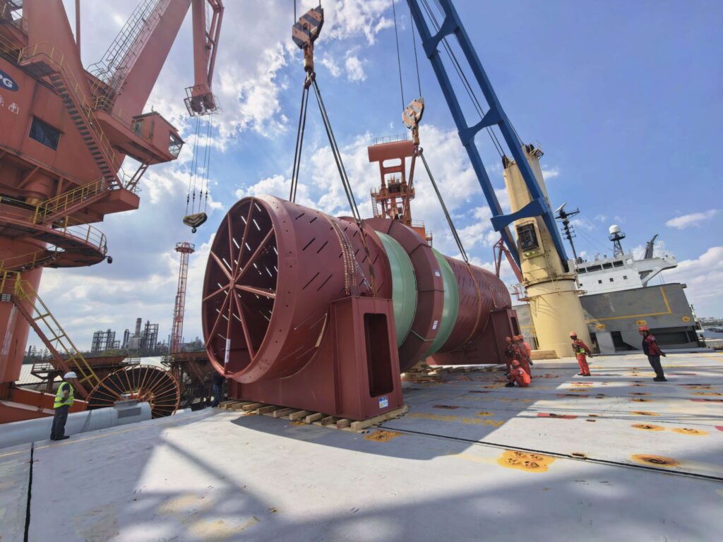 170-ton industrial drum secured on the deck of a heavy-lift vessel while cranes and stevedores complete cargo handling operations at the port.