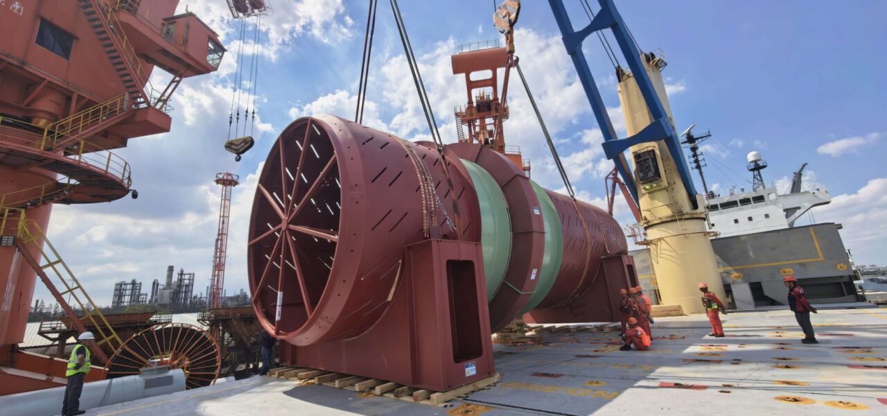 170-ton industrial drum secured on the deck of a heavy-lift vessel while cranes and stevedores complete cargo handling operations at the port.